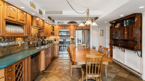 A spacious kitchen with wooden cabinets, a central island, and a dining area with a large wooden table and chairs. - Columbine 2107 (Crested Butte)
