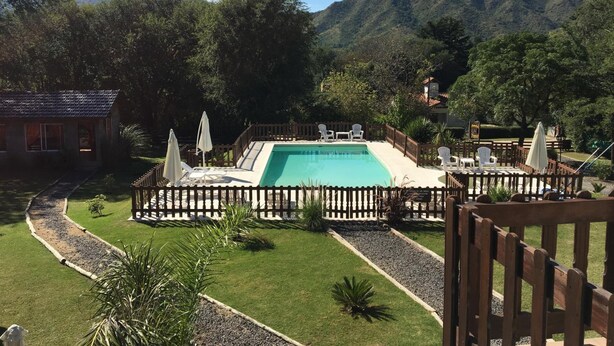 A swimming pool surrounded by a wooden fence, with chairs and umbrellas for relaxation.