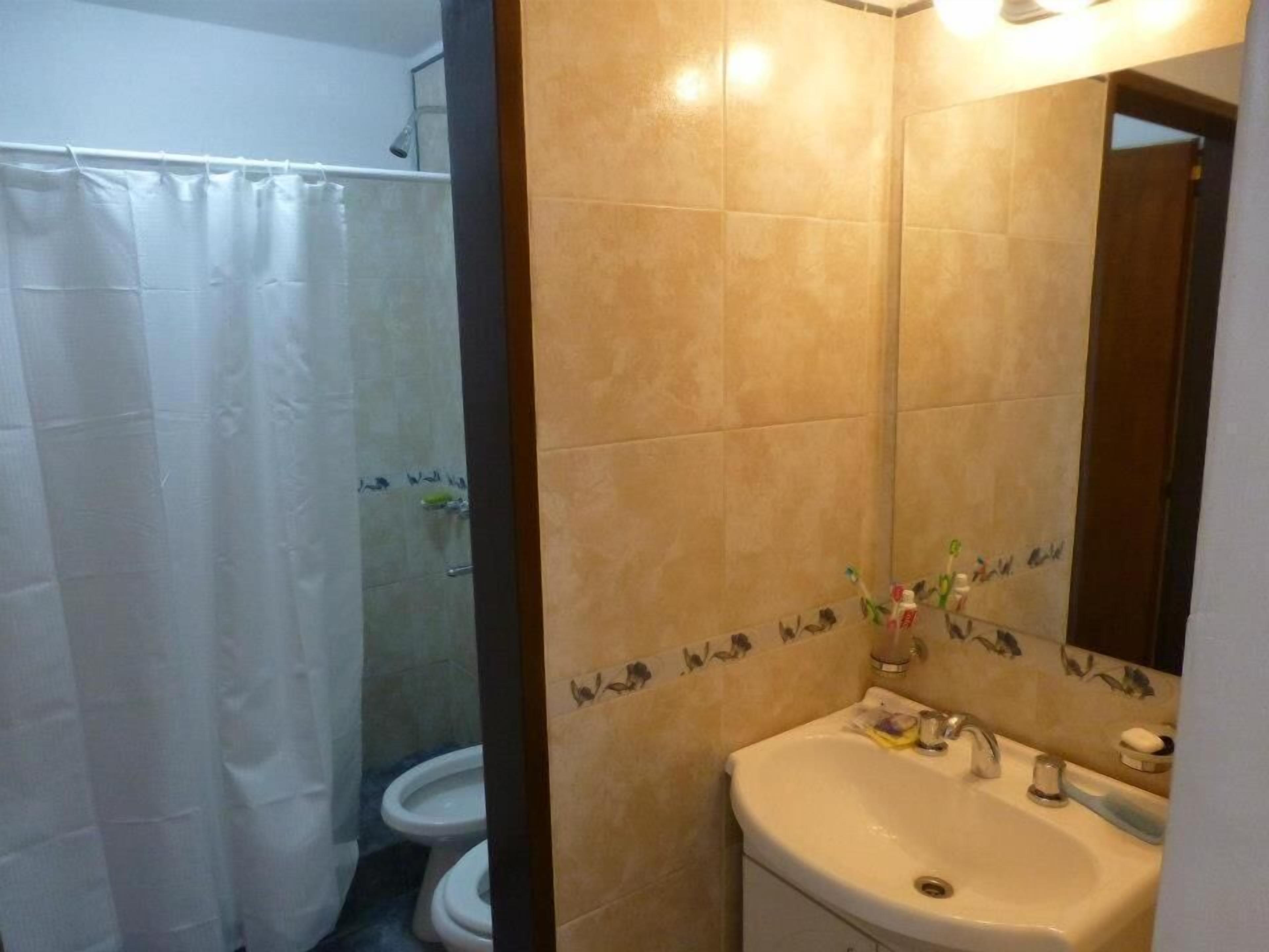 Un baño con cortina de ducha, inodoro y lavamanos con espejo.