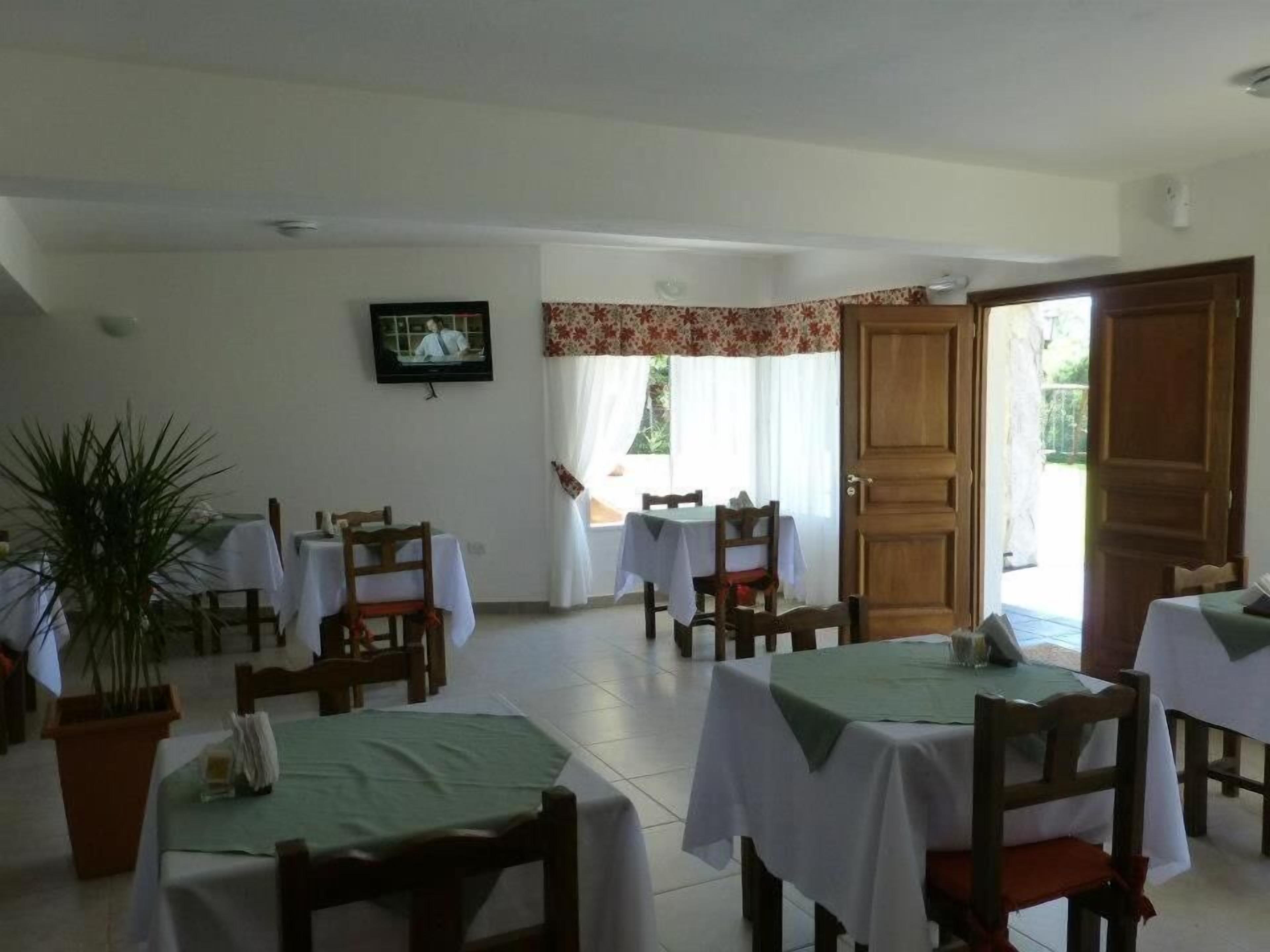 A dining area with tables and chairs, a television on the wall, and a door leading outside.