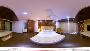 A modern hotel room with a curved bed, a ceiling fan, a TV, and a seating area with a chair. - Hotel Blossoms (Tiruchirappalli)