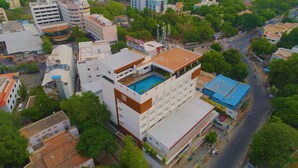 A hotel with a rooftop pool, surrounded by other buildings and trees. - Hotel Blossoms (Tiruchirappalli)