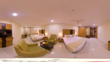 A hotel room with a large bed, two sofas, a TV, and a desk with a chair.
