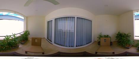 A room with a curved ceiling, a sliding glass door with curtains, two beige sofas, and potted plants.