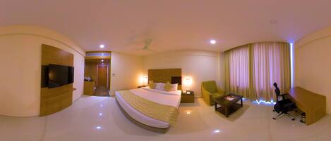 A hotel room with a large bed, a desk, a chair, a TV, and a ceiling fan.