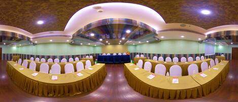 A conference room with multiple round tables, white chairs, and a stage with a blue backdrop.