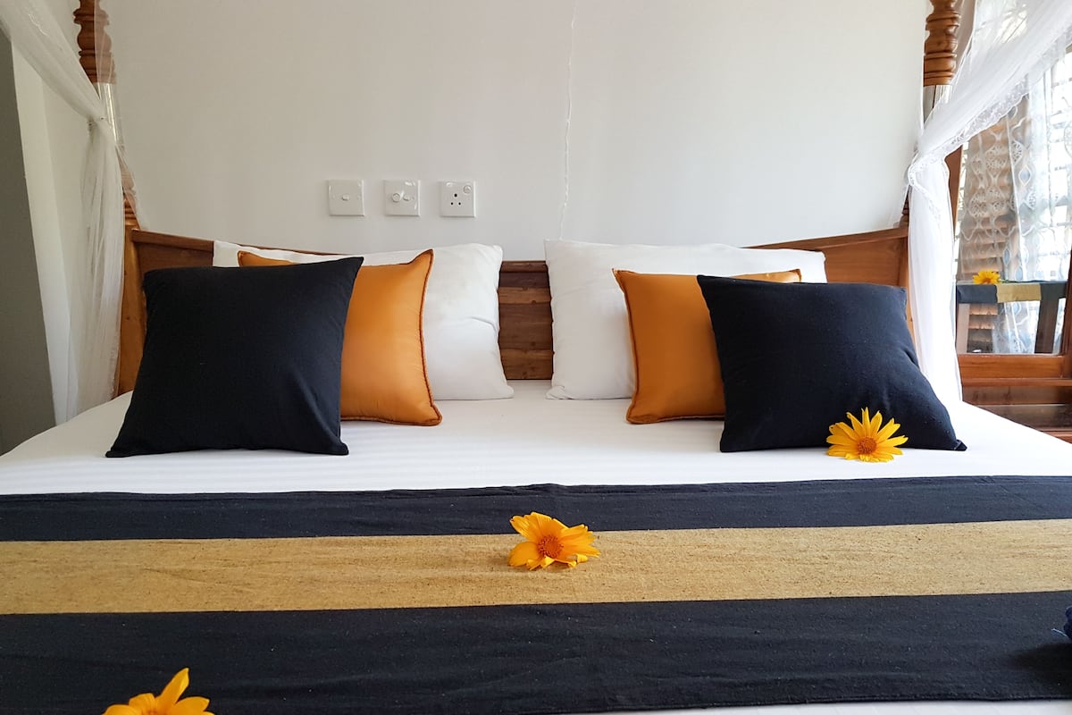 A bed with white bedding, black and orange pillows, and a black and beige bed runner.