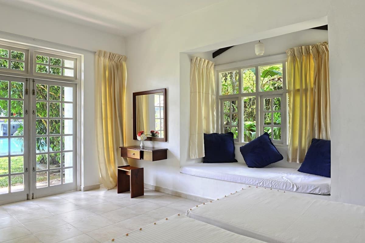 A room with a bed, a bedside table with a mirror, and a window with curtains.