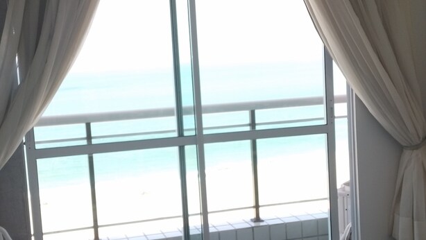 A room with a large window overlooking a beach.