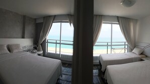A hotel room with two beds, a view of the beach, and a large window with curtains.