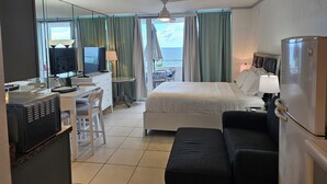 A hotel room with a bed, a desk with a computer, a refrigerator, and a view of the sea. - Beachfront Studio  overlooking the Atlantic Ocean (Fort Lauderdale Beach)