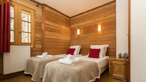 A wooden-paneled room with two beds, each with a red pillow and a rolled towel.