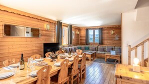 A wooden interior with a dining table set for two, a sofa, and a TV.