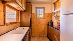 A kitchen with wooden cabinets, a double sink, a window with a view, and a refrigerator.