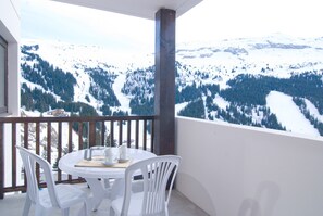 Un balcon avec une table et des chaises, donnant sur un paysage montagneux enneigé.