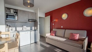 Un espacio habitable compacto con kitchenette, un sofá con cojines rojos y una zona de comedor.