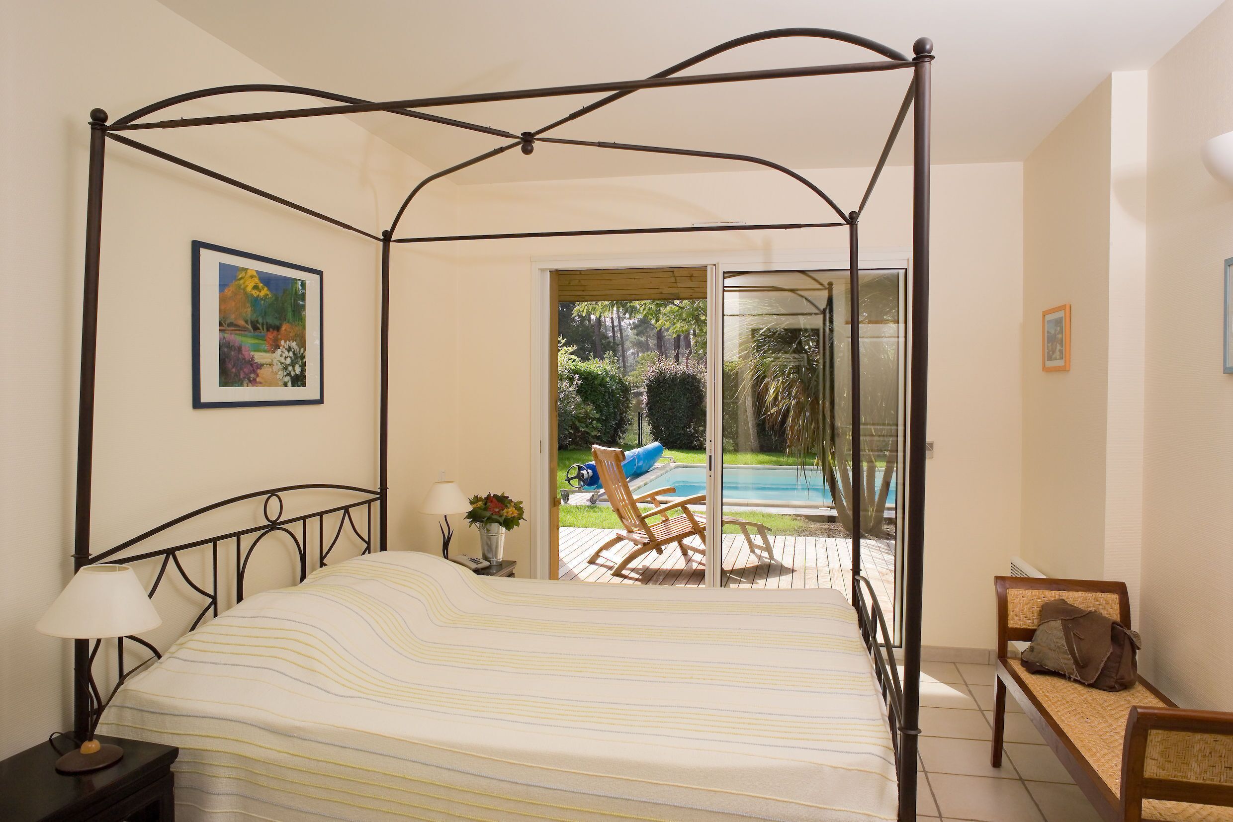 A four-poster bed with a view of a swimming pool and garden.