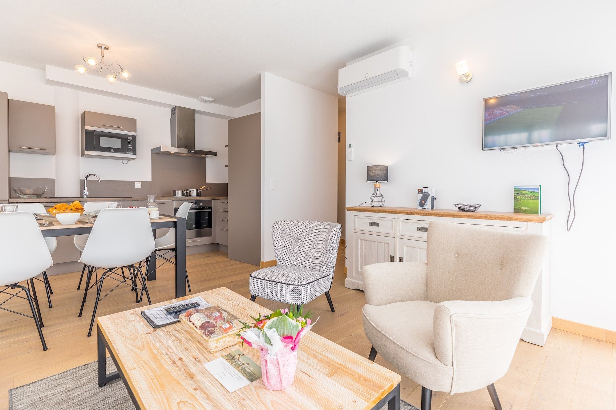 A modern kitchen with a dining area, a TV mounted on the wall, and a cozy seating arrangement.