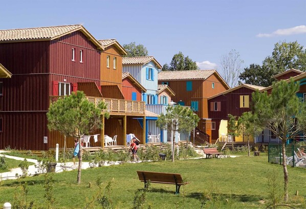 A row of colorful wooden cabins with a grassy yard and a bench.