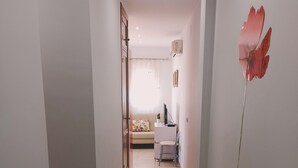 A narrow hallway with a tiled floor leading to a room with a bed, a desk, and a window with a curtain. - Terrace with Breathtaking Views - Apartment Sebastian (conil de la frontera)
