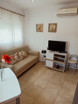 Ein Wohnzimmer mit einer Couch, einem Fernsehschrank und einem kleinen Tisch mit einer Vase.