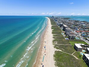 An aerial view of a coastal city with a long beach, buildings, and a clear blue sky. - Fun Family Condo on the Beach next to Heated Pools! (South Padre Island)