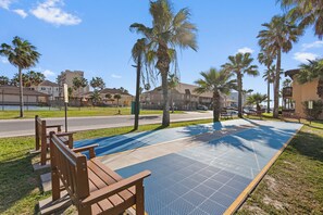 A park area with a blue tactile paving path, wooden benches, and palm trees.