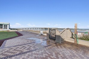 A paved walkway leading to a gated entrance with a view of the sea and a bridge in the background.