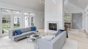 A spacious living room with a fireplace, a grey sofa, and a dining area with a table and chairs. - Stunning Hampton Holiday Family Fantasy for your Team  (East Hampton)