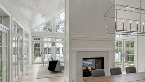 A spacious room with a large wooden dining table, grey chairs, a fireplace, and a modern chandelier. - Stunning Hampton Holiday Family Fantasy for your Team  (East Hampton)