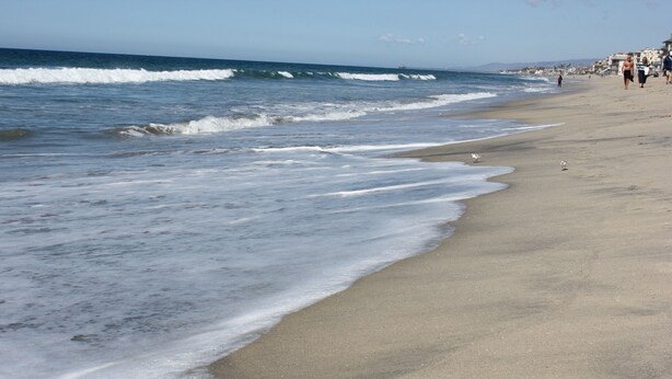 A beach with waves, a sandy shore, and buildings in the background. - OCEAN VIEW, 1BR, OUTSTANDING LOCATION F (Carlsbad)