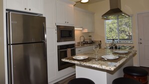 A modern kitchen with stainless steel appliances, granite countertops, and a window with blinds. - OCEAN VIEW, 1BR, OUTSTANDING LOCATION F (Carlsbad)