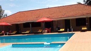 A swimming pool with lounge chairs and umbrellas, a tiled roof, and a tiled floor. - Golden Peace Hotel (Gulu)