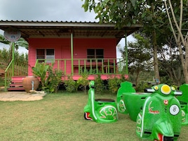 Una casa rosa con porche verde y una maceta grande en los escalones.