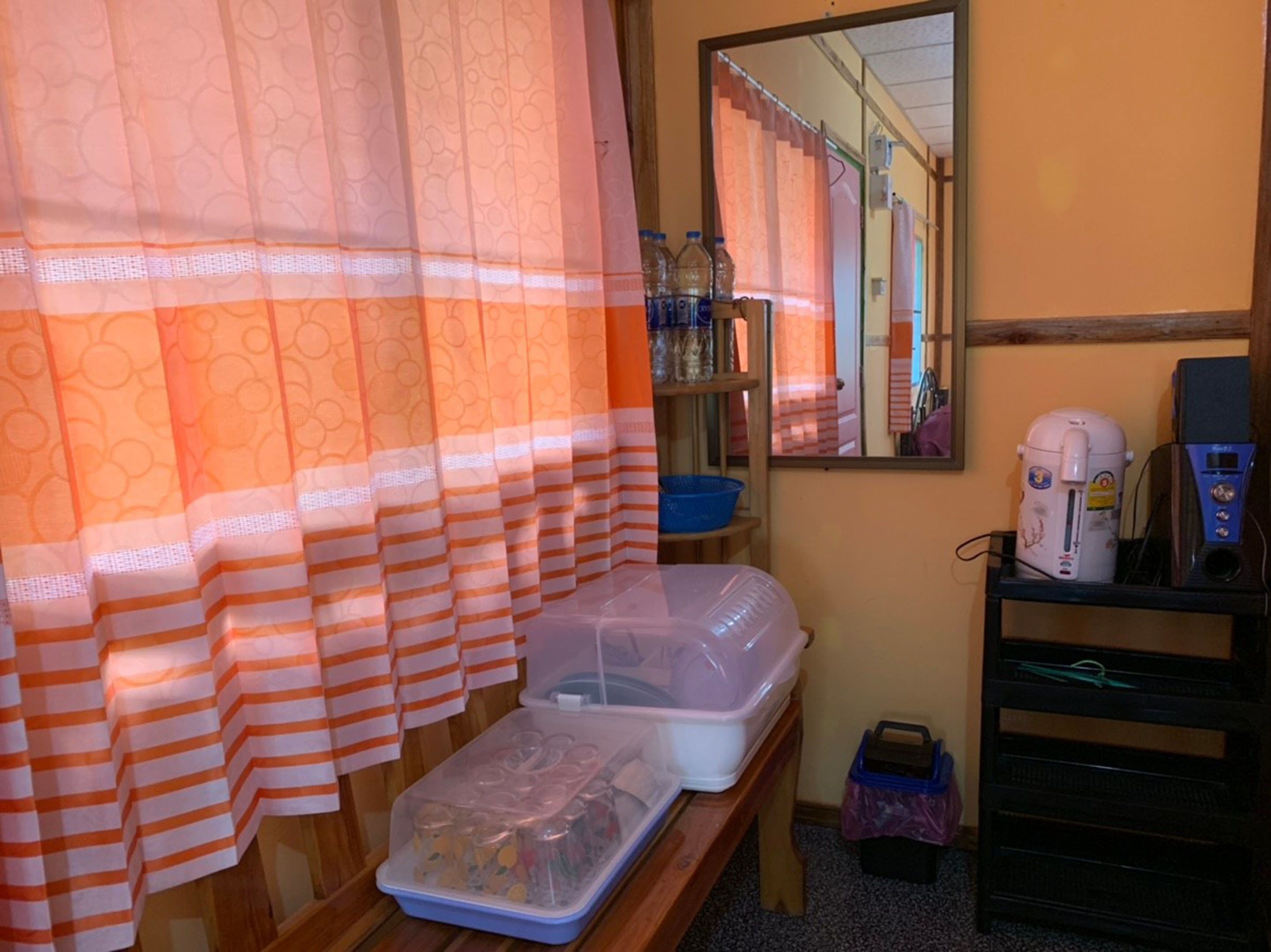 Un baño con cortina de ducha, un espejo, un lavabo, una cafetera y un recipiente de plástico en un estante.