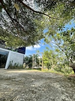 Un espacio pavimentado con un edificio de diseño moderno, una estructura de madera y abundante vegetación.
