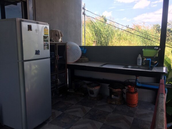 A compact kitchen with a refrigerator, sink, and a window overlooking greenery. - At Trin Khao Kho (Khao Kho)