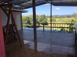 Un espacio al aire libre techado con piso de baldosas, una escalera de madera y vista a un paisaje verde.