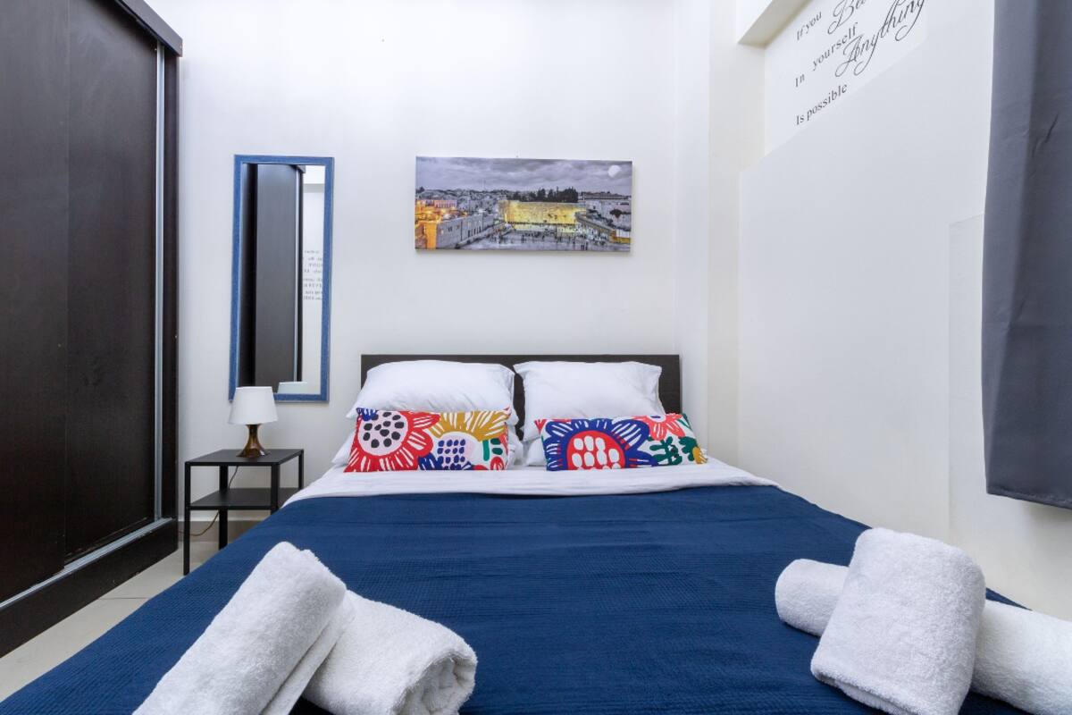 Une chambre d’hôtel avec un lit, des oreillers, une table de chevet, une lampe, un tableau encadré au mur et une grande fenêtre.