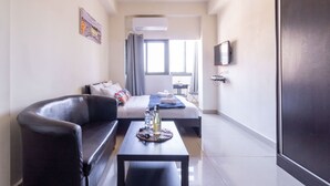 A modern hotel room with a sofa, a bed, a TV, and a window. - NHE Machne Yehuda Apartments (Jerusalem)
