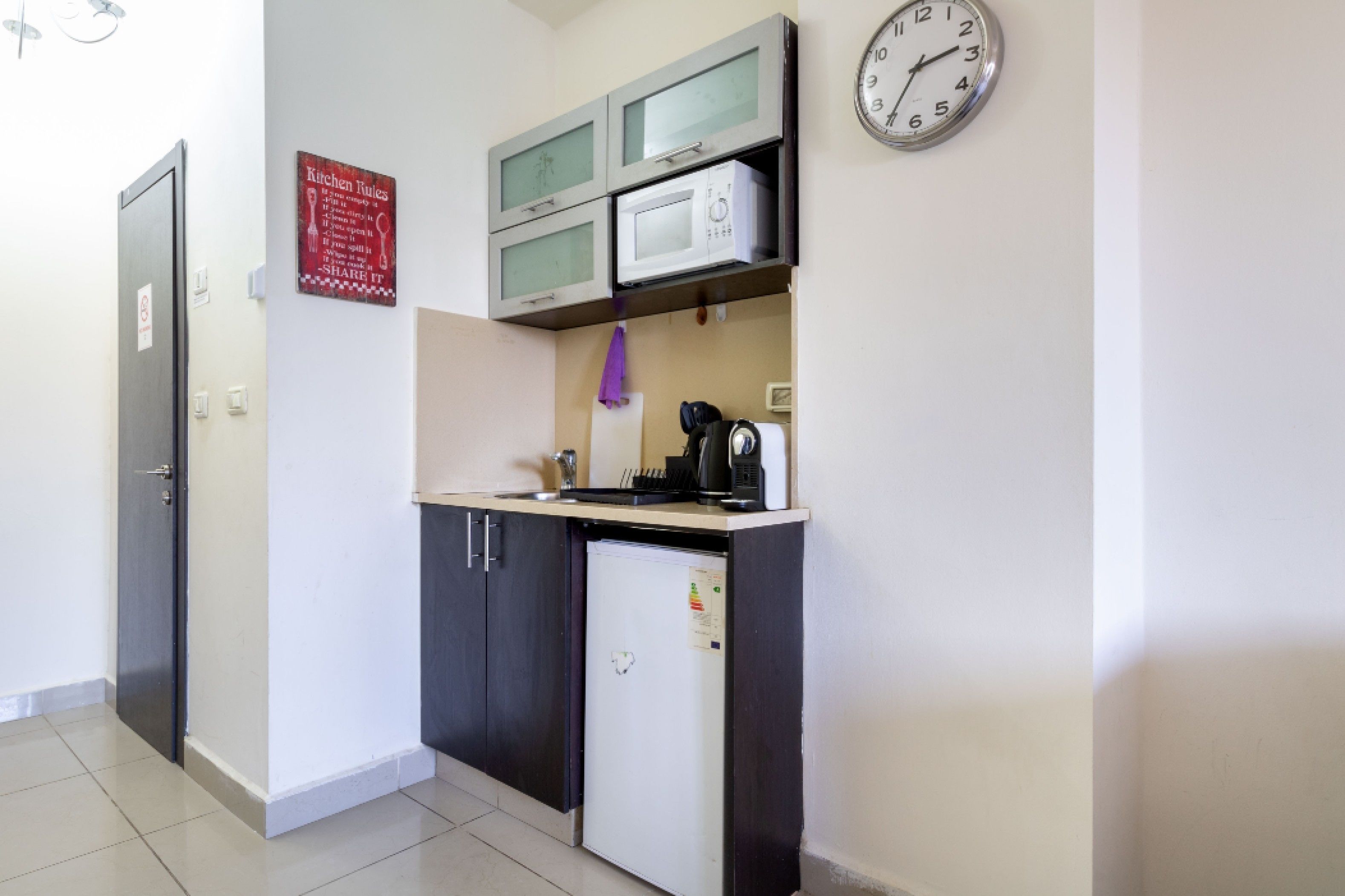 Una cocina compacta con microondas, refrigerador y un reloj en la pared.