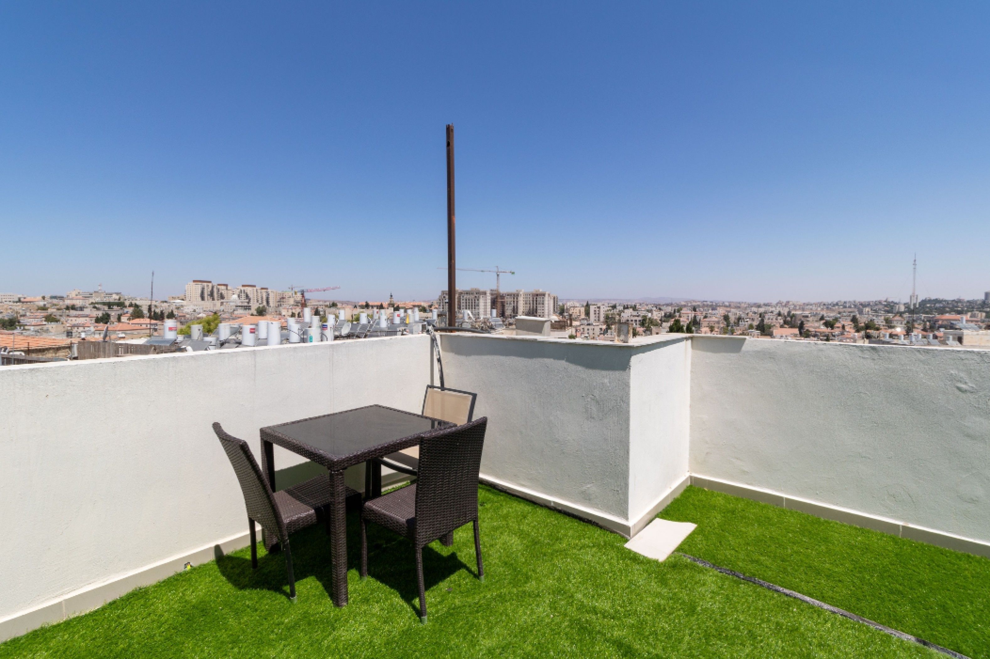 A rooftop terrace with a table and chairs, a view of the cityscape, and a tall chimney.
