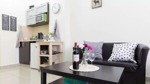 A compact living space with a kitchenette, a dining table with a bottle of wine, and a sofa with patterned pillows. - NHE Machne Yehuda Apartments (Jerusalem)