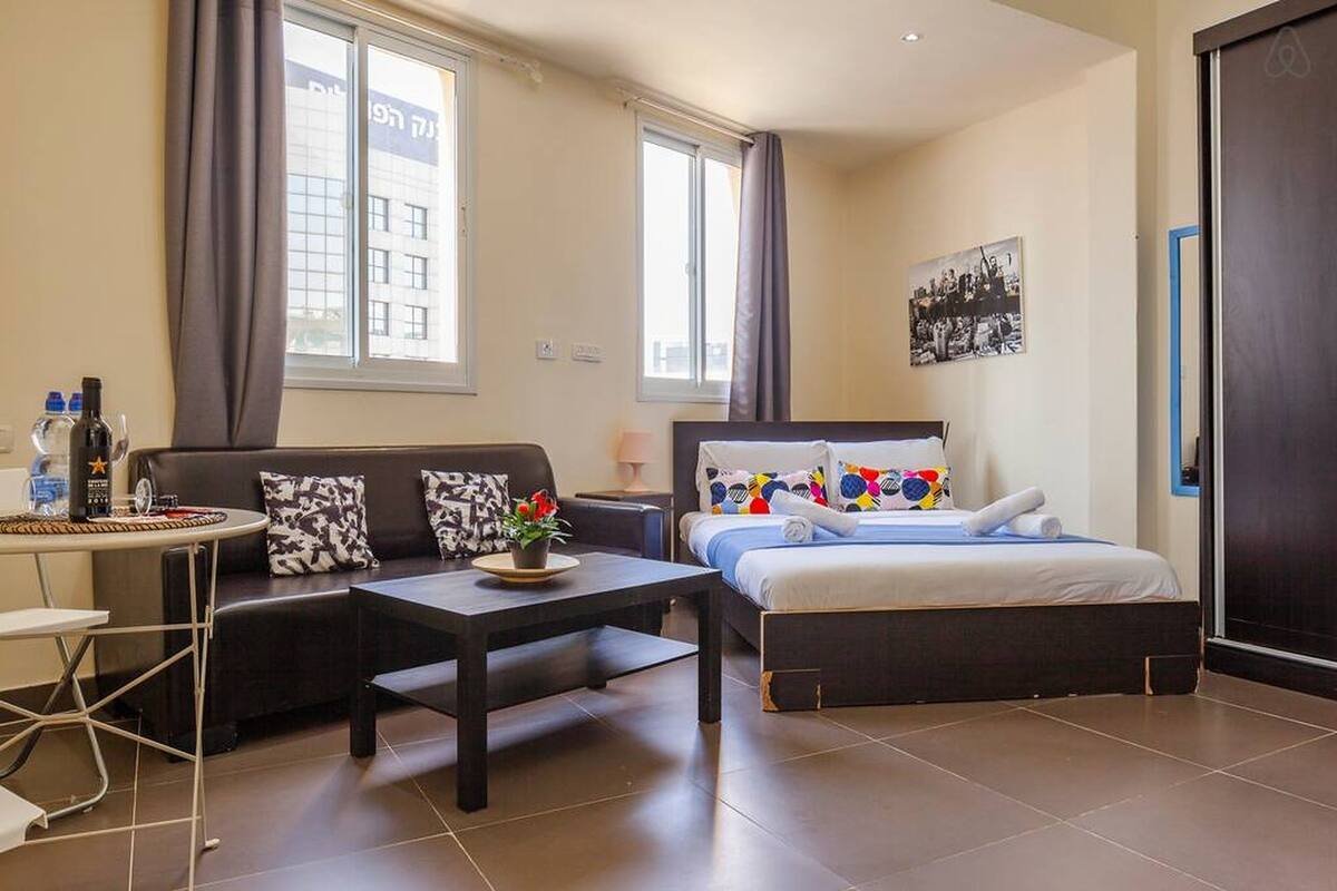 A hotel room with a bed, a sofa, a small table, and a window.
