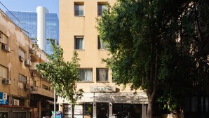 A street view with a building that has a sign in a foreign language, a tree in front, and a scooter parked on the sidewalk. - NHE Rothschild Apartments (Tel Aviv)