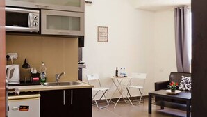 A compact kitchen with a microwave, kettle, and small refrigerator. There is a dining area with a table and chairs, and a sofa in the living room. - NHE Rothschild Apartments (Tel Aviv)