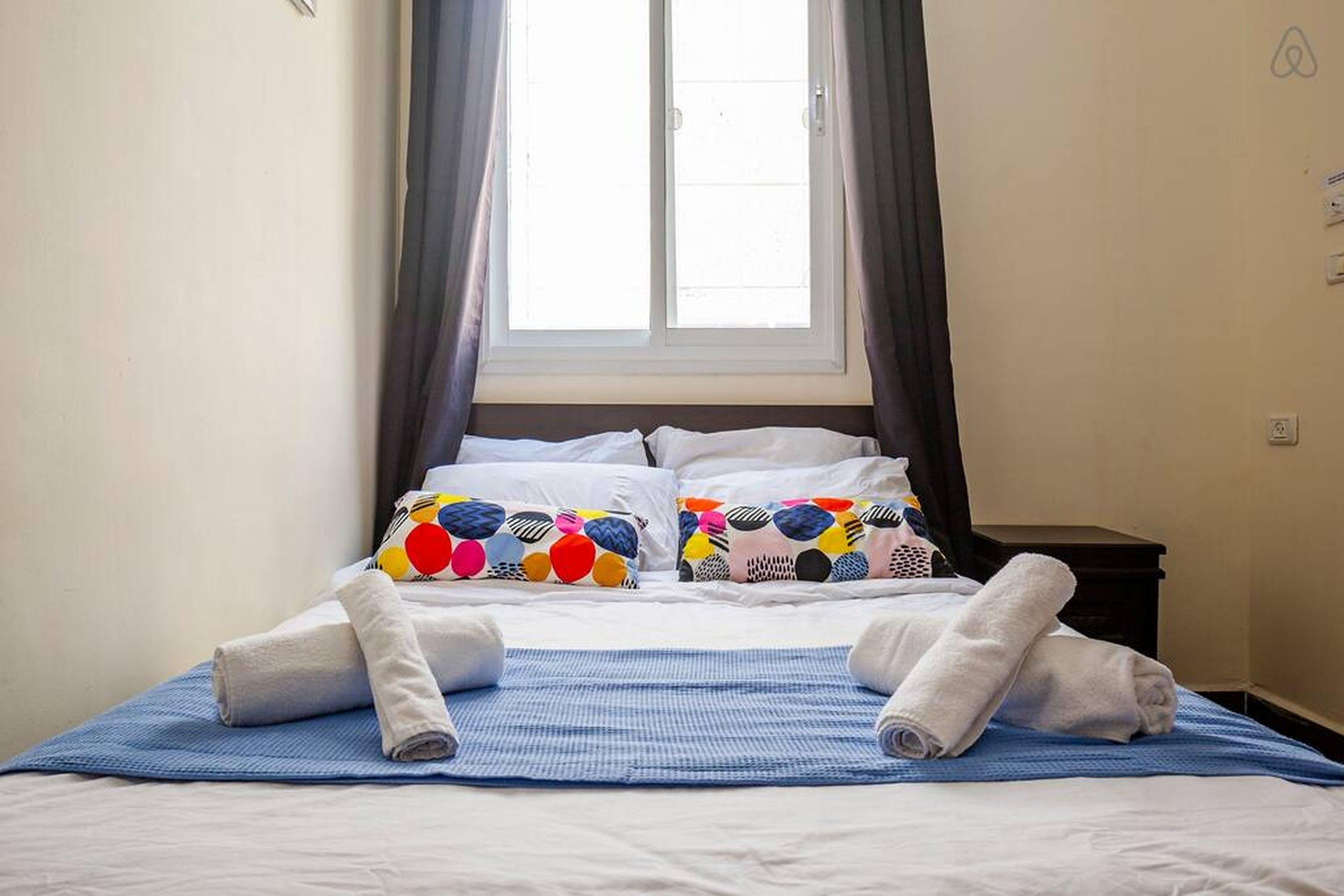 A neatly made bed with white linens, colorful pillows, and a blue blanket.