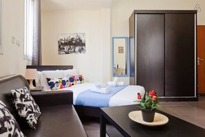 Ett hotellrum med en säng, en soffa, ett bord med en växt, en garderob och ett inramat foto på väggen.