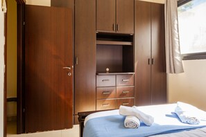 A hotel room with a large wardrobe, a bed with blue bedding, and a window with curtains. - NHE Rothschild's Corner (Tel Aviv)