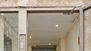 Un couloir étroit, avec une porte fermée au fond, une porte en verre sur la gauche et un cadre de porte en métal.